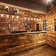 Die rustikale Bar des Hotels Bretterbude in Büsum mit Ziegelwand, Theke aus groben Holzplanken und Glühbirnenbeleuchtung